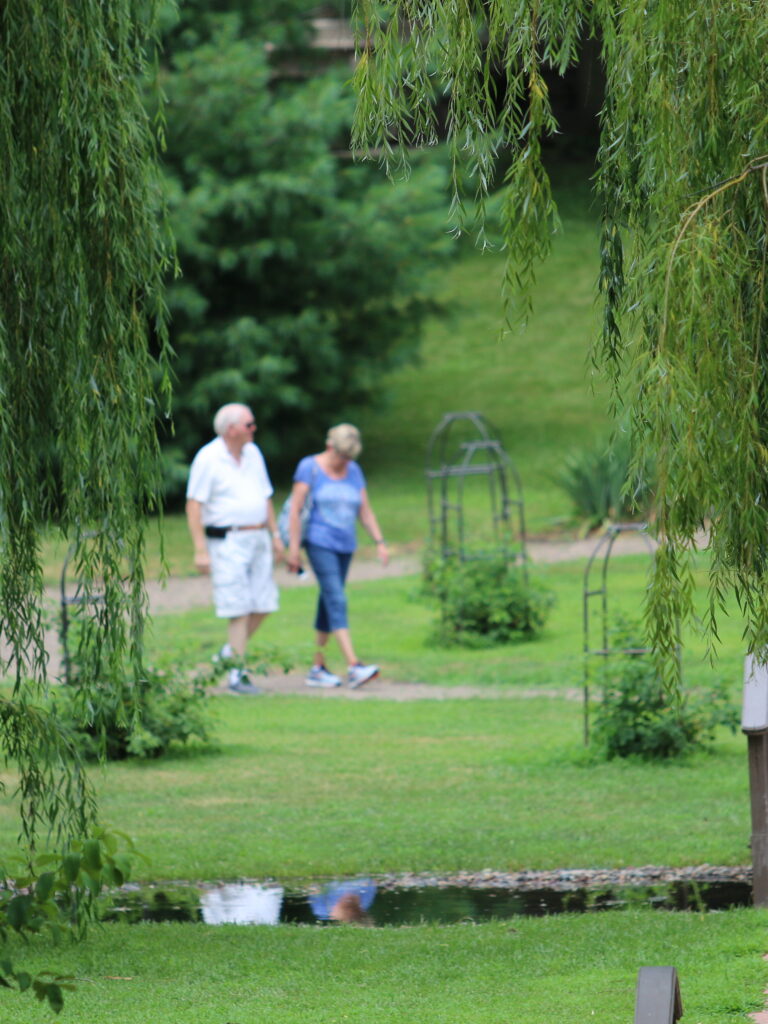 an older couple walking down a path in a garden hand in hand