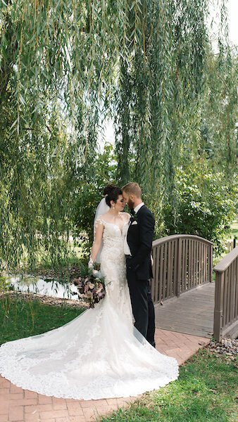 A newly wed couple posing by a small body of water and a small bridge